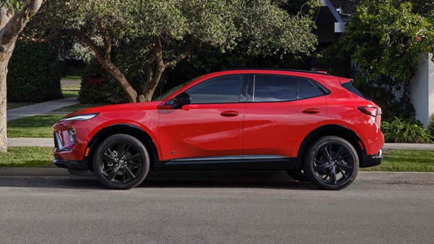 Red 2026 Buick Envision parked along a residential street, shown in side profile with black wheels and trees in the background.