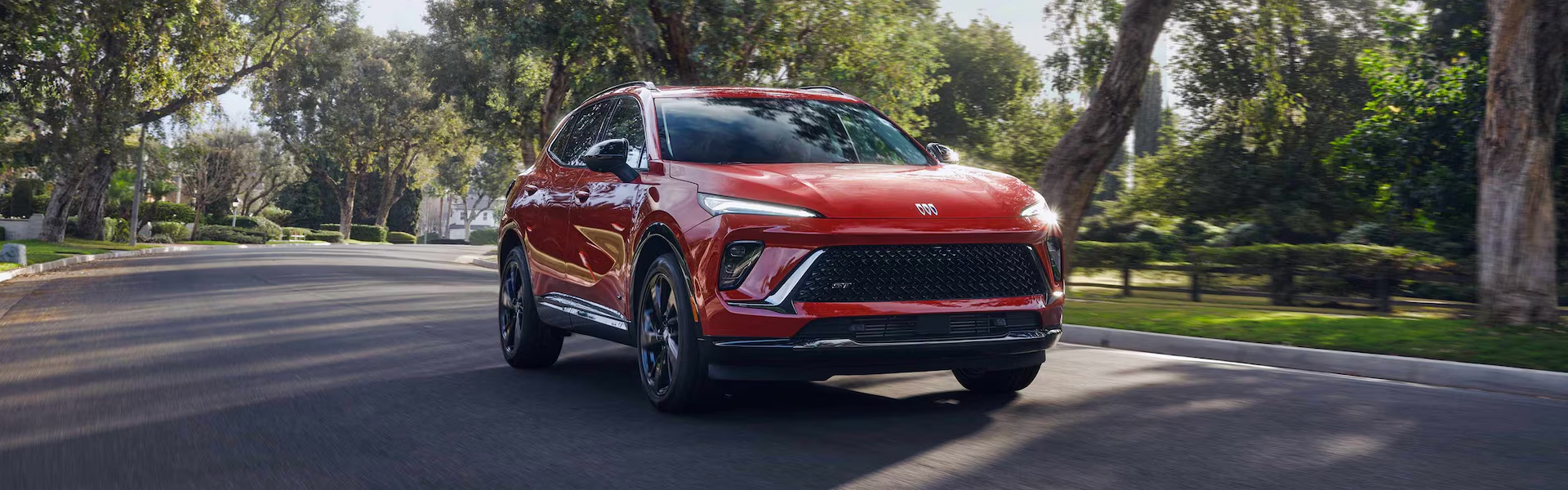 2026 Buick Envision SUV in red driving on a scenic tree-lined road.